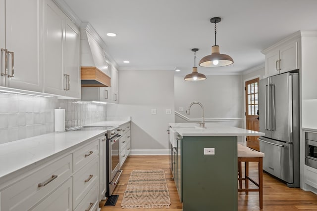 kitchen with tasteful backsplash, sink, high end appliances, an island with sink, and white cabinets