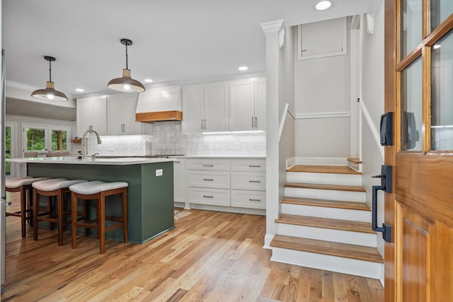 kitchen with white cabinets, light hardwood / wood-style floors, premium range hood, hanging light fixtures, and backsplash