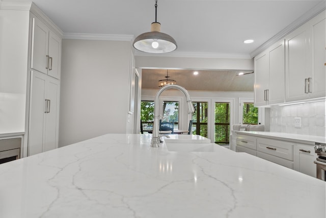 kitchen featuring backsplash, pendant lighting, ornamental molding, white cabinets, and light stone counters