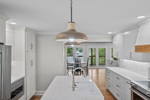 kitchen featuring premium appliances, sink, white cabinetry, and pendant lighting