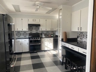 kitchen featuring extractor fan, range with two ovens, black fridge, decorative backsplash, and white cabinets