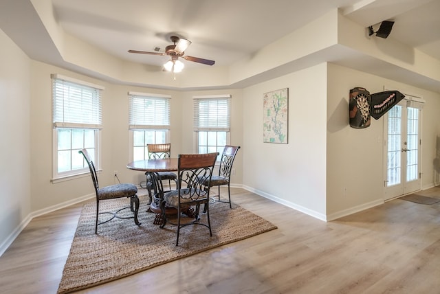 dining space with ceiling fan, a raised ceiling, light wood-type flooring, and french doors