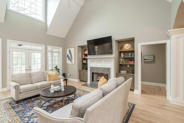 living room featuring french doors, a towering ceiling, built in shelves, ceiling fan, and light hardwood / wood-style floors