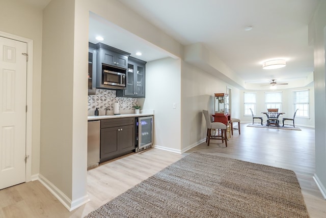 kitchen with light wood-type flooring, tasteful backsplash, stainless steel appliances, beverage cooler, and ceiling fan