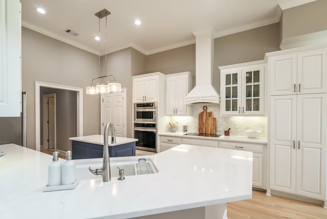 kitchen with custom exhaust hood, a kitchen island with sink, hanging light fixtures, decorative backsplash, and white cabinetry