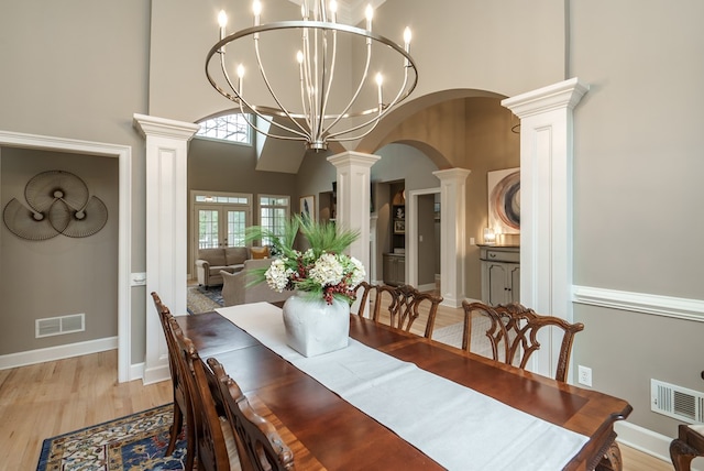 dining area with a notable chandelier, light hardwood / wood-style floors, a high ceiling, and decorative columns