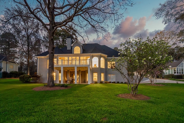 back house at dusk with a lawn and a balcony