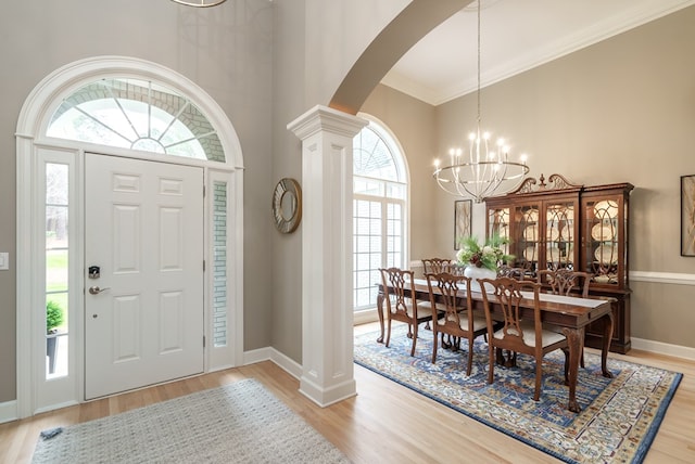 foyer entrance featuring decorative columns, an inviting chandelier, ornamental molding, and light hardwood / wood-style flooring