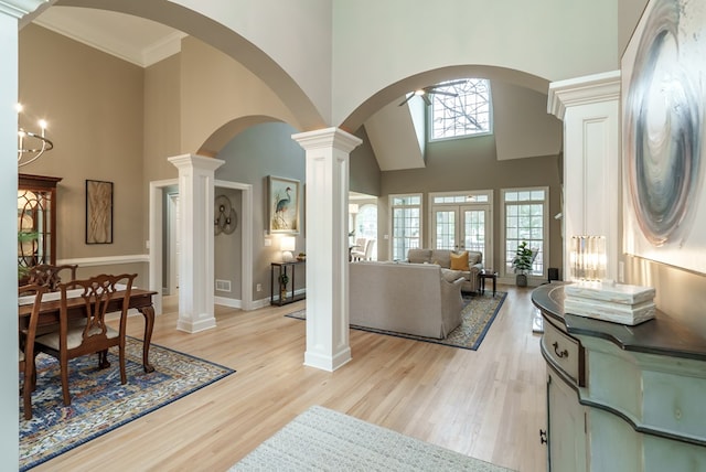 living room with light wood-type flooring, decorative columns, crown molding, a chandelier, and a high ceiling