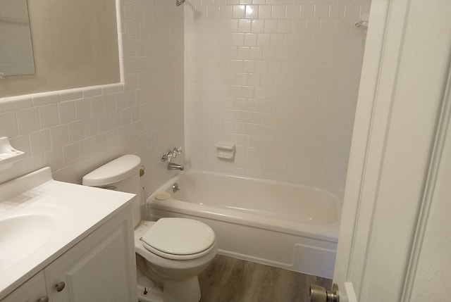 full bathroom featuring vanity, hardwood / wood-style flooring, tiled shower / bath combo, toilet, and tile walls