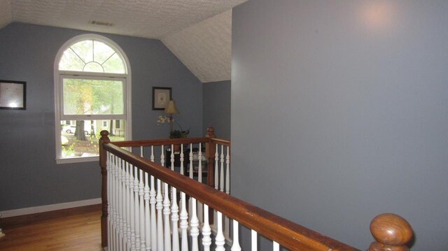 131 NE Carriage Ct, Milledgeville, GA 31061 - hall with visible vents, an upstairs landing, a textured ceiling, vaulted ceiling, and wood finished floors