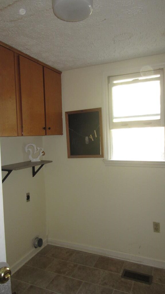 131 NE Carriage Ct, Milledgeville, GA 31061 - clothes washing area featuring hookup for an electric dryer, baseboards, a textured ceiling, visible vents, and cabinet space