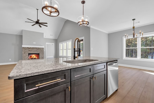 kitchen with dishwasher, a kitchen island with sink, sink, a brick fireplace, and light stone countertops