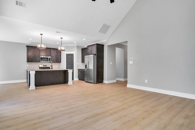 kitchen with decorative backsplash, appliances with stainless steel finishes, dark brown cabinets, decorative light fixtures, and an island with sink