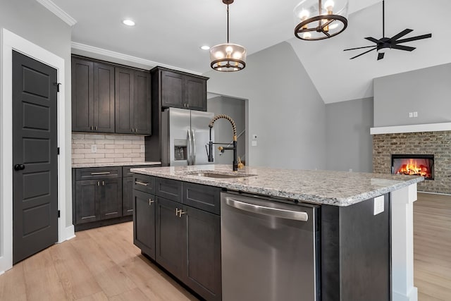 kitchen with stainless steel appliances, sink, pendant lighting, a fireplace, and an island with sink