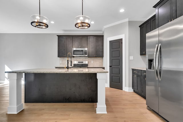 kitchen with pendant lighting, stainless steel appliances, and an island with sink