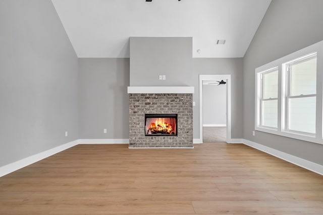 unfurnished living room with ceiling fan, a fireplace, vaulted ceiling, and light wood-type flooring