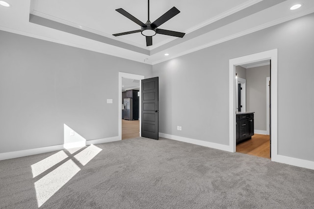 unfurnished bedroom with ensuite bathroom, ceiling fan, a raised ceiling, and light carpet