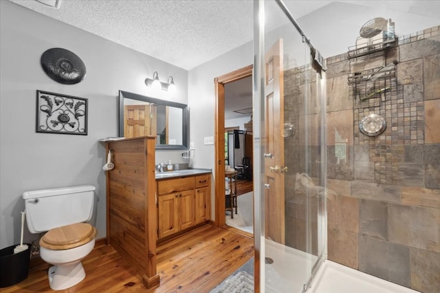 bathroom featuring a textured ceiling, a shower stall, toilet, wood finished floors, and vanity