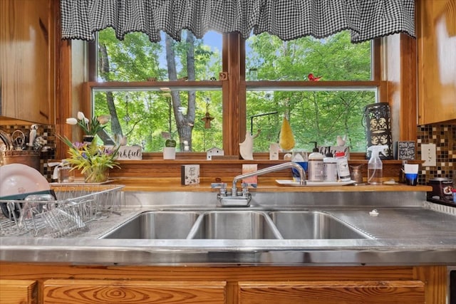kitchen featuring stainless steel counters, a sink, brown cabinets, and a wealth of natural light
