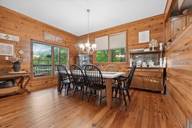 dining space with wooden walls, hardwood / wood-style flooring, and a chandelier