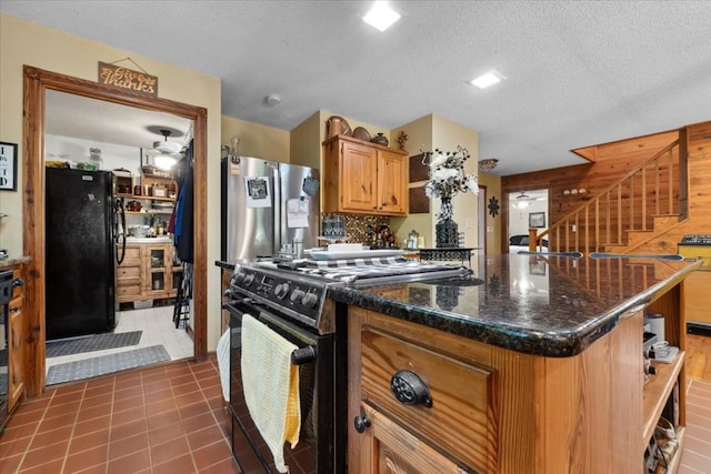 kitchen featuring dark stone countertops, open shelves, brown cabinetry, black appliances, and a textured ceiling