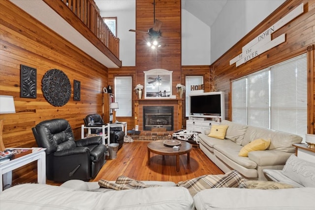 living room featuring hardwood / wood-style floors, wood walls, ceiling fan, a fireplace, and high vaulted ceiling