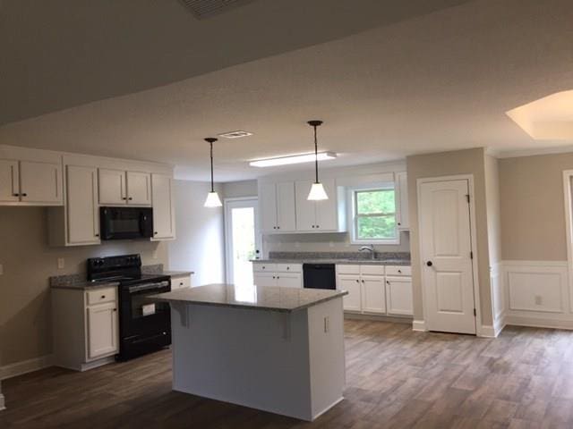 kitchen featuring dark wood finished floors, a sink, black appliances, white cabinetry, and a center island