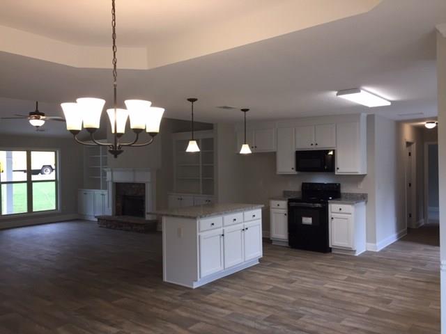 kitchen with dark wood-style floors, a fireplace with raised hearth, black appliances, white cabinetry, and open floor plan