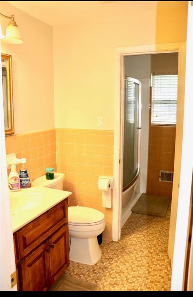 bathroom featuring vanity, toilet, a shower with door, and tile walls