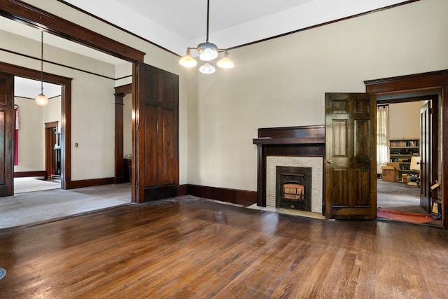 unfurnished living room featuring hardwood / wood-style floors, a notable chandelier, and a brick fireplace