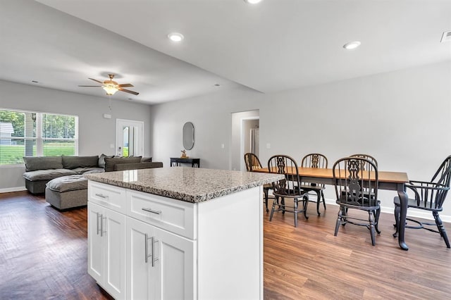 kitchen with a center island, dark wood-type flooring, ceiling fan, light stone countertops, and white cabinetry