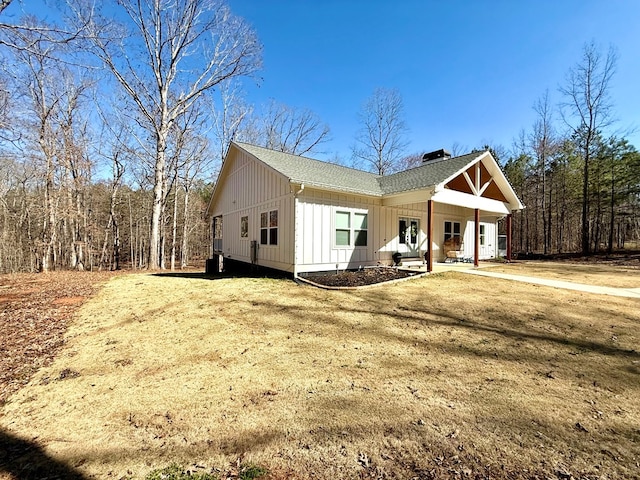 view of front of property featuring a shingled roof, driveway, board and batten siding, a chimney, and a front yard