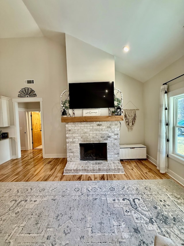 unfurnished living room with visible vents, baseboards, light wood-style flooring, a brick fireplace, and high vaulted ceiling