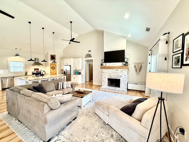 living area with light wood finished floors, visible vents, a fireplace with raised hearth, a baseboard radiator, and ceiling fan