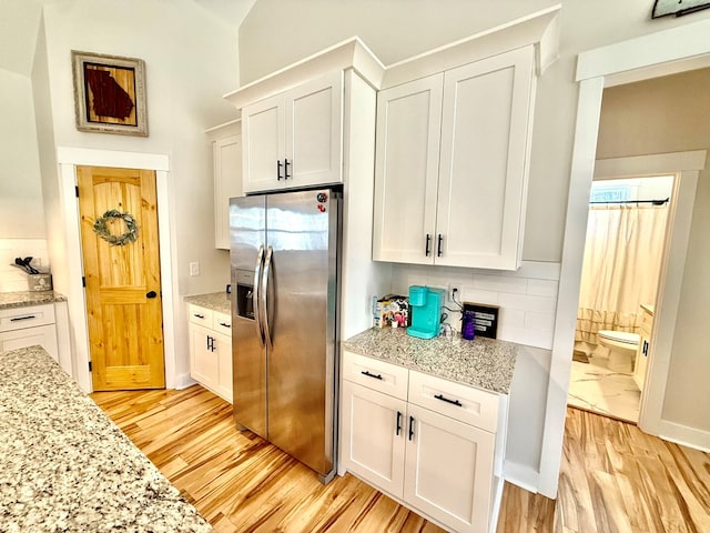 kitchen featuring light wood finished floors, tasteful backsplash, light stone countertops, white cabinetry, and stainless steel refrigerator with ice dispenser