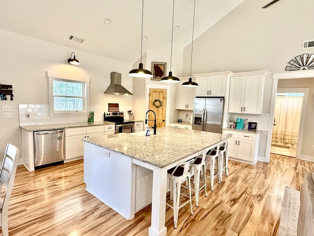 kitchen featuring appliances with stainless steel finishes, an island with sink, ventilation hood, and white cabinets