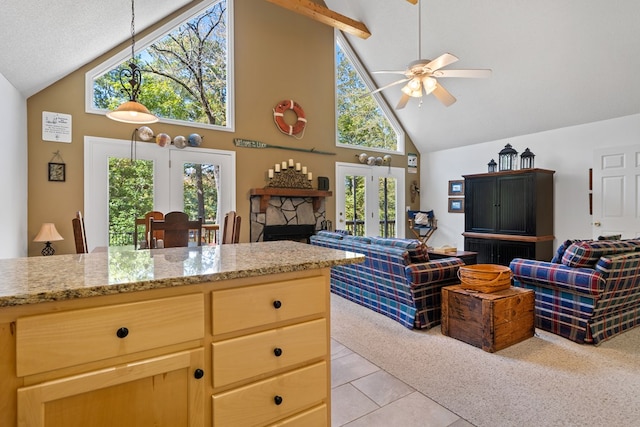 kitchen featuring a stone fireplace, ceiling fan, light tile patterned floors, and high vaulted ceiling