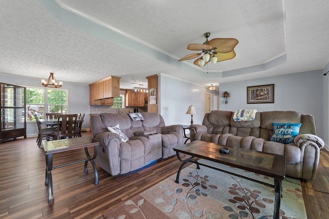 living room featuring a textured ceiling, dark wood finished floors, a tray ceiling, a chandelier, and a ceiling fan