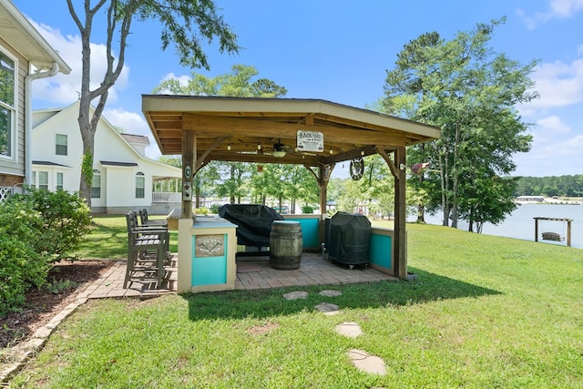 view of grassy yard featuring ceiling fan, a gazebo, and a water view