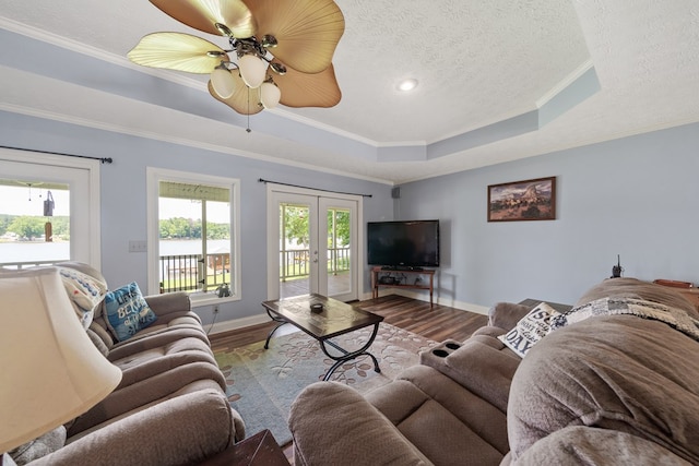 living area with wood finished floors, a raised ceiling, baseboards, ornamental molding, and a textured ceiling