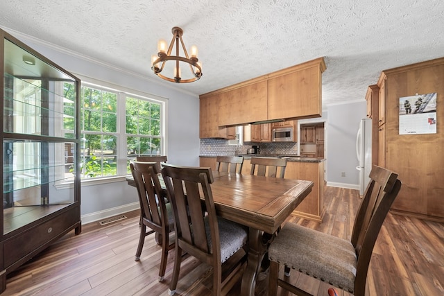 dining room with baseboards, a chandelier, ornamental molding, wood finished floors, and a textured ceiling