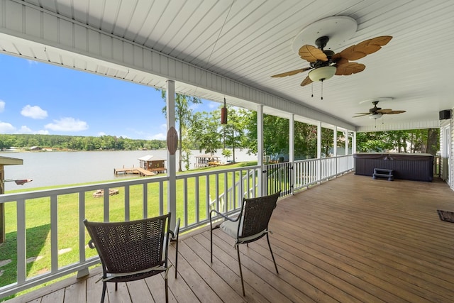 wooden deck featuring a hot tub, a water view, ceiling fan, and a lawn