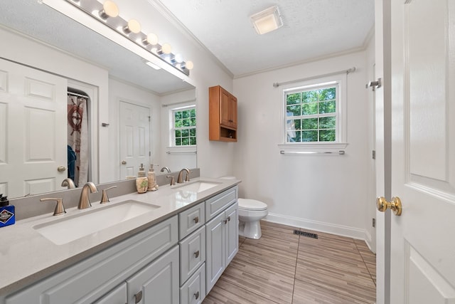 full bath with plenty of natural light, baseboards, toilet, ornamental molding, and double vanity