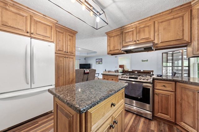 kitchen with white fridge, stainless steel range with gas cooktop, under cabinet range hood, dark wood finished floors, and a textured ceiling