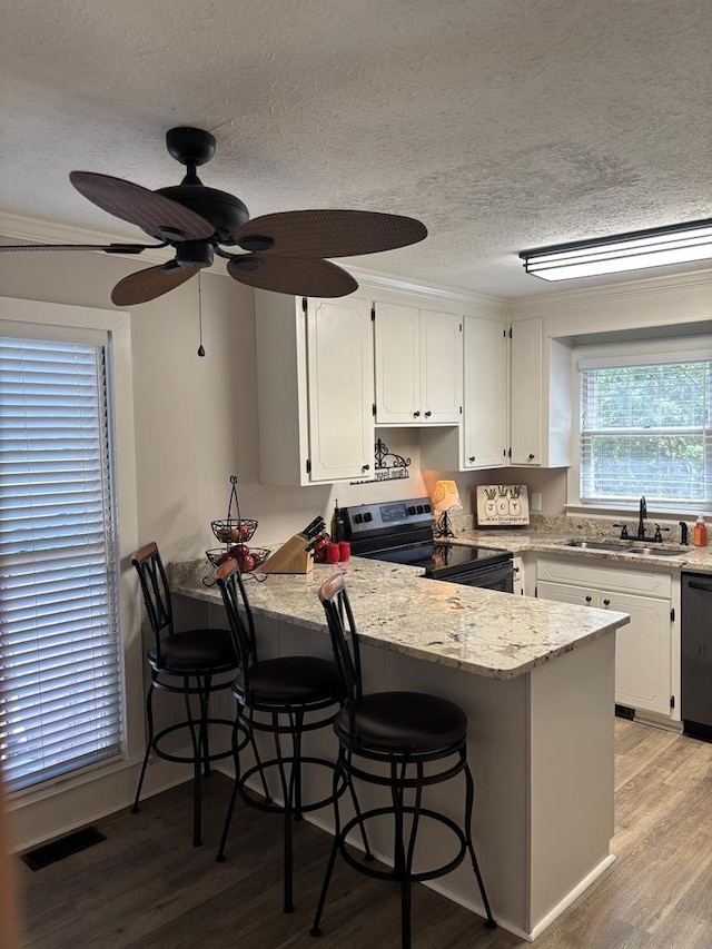kitchen with stainless steel range with electric cooktop, a sink, a peninsula, white cabinetry, and a textured ceiling