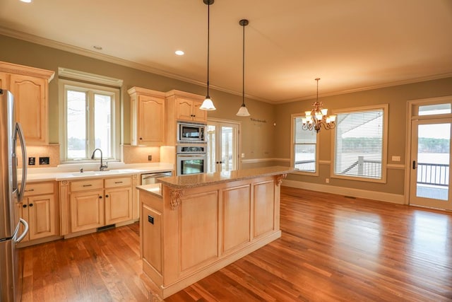 kitchen with light brown cabinetry, a sink, appliances with stainless steel finishes, a notable chandelier, and a center island