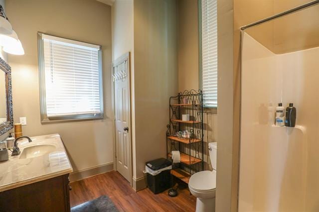 bathroom featuring toilet, wood finished floors, a shower, baseboards, and vanity