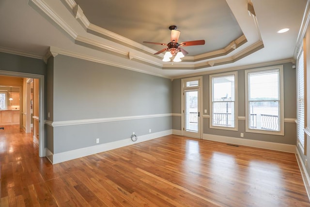 unfurnished room featuring wood finished floors, a ceiling fan, visible vents, baseboards, and a tray ceiling