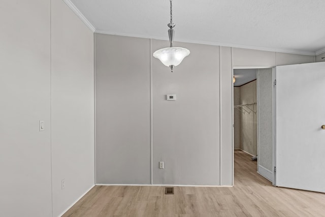 unfurnished dining area with ornamental molding, a textured ceiling, and light wood-type flooring